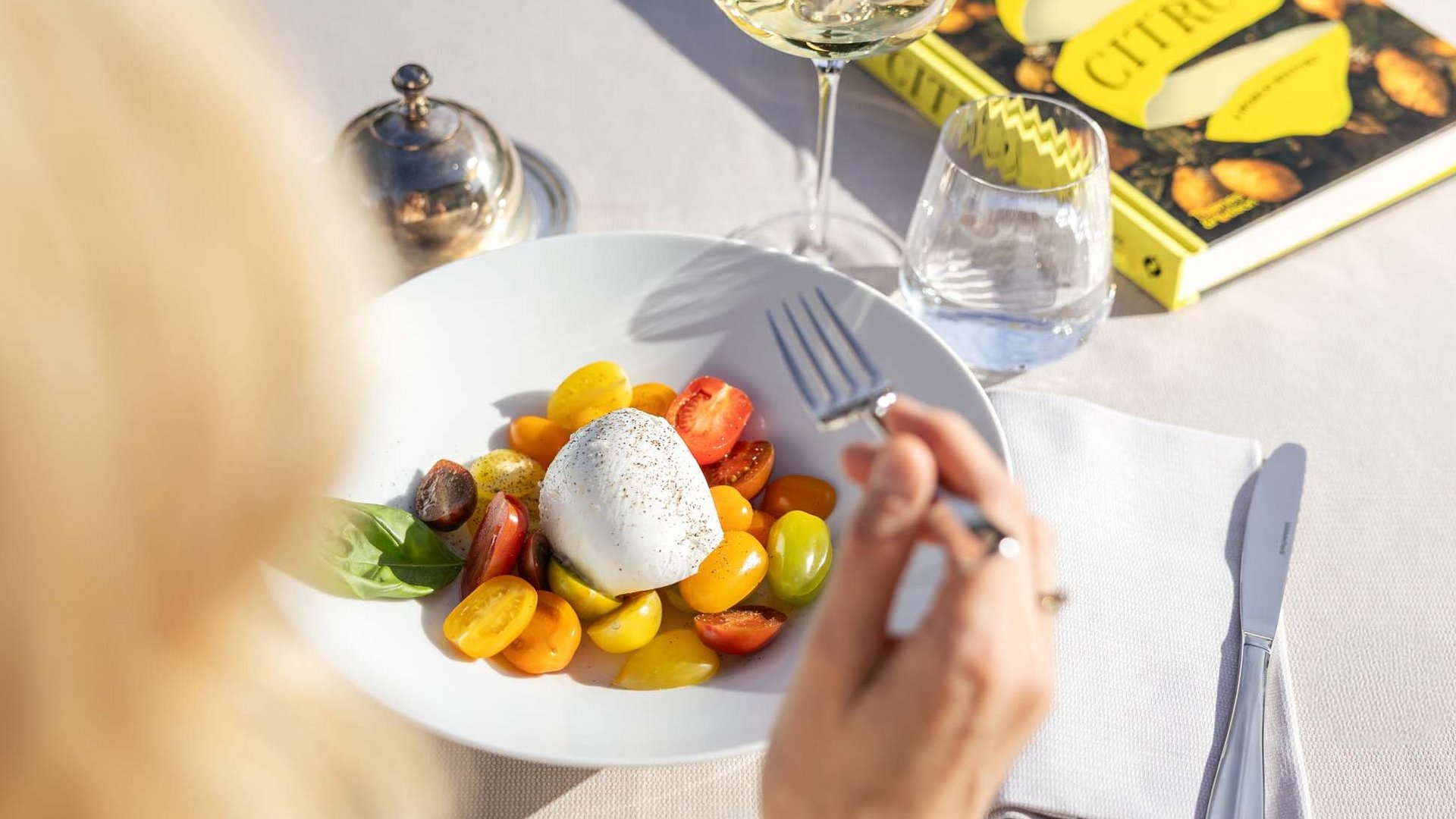 Lingers’ dine-around concept Person eating tomato salad with mozzarella and drinking white wine at table