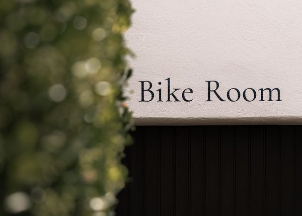Lingers – Ihr Hotel in Girlan Schild mit der Aufschrift Bike Room an einer weißen Wand neben grünen Pflanzen