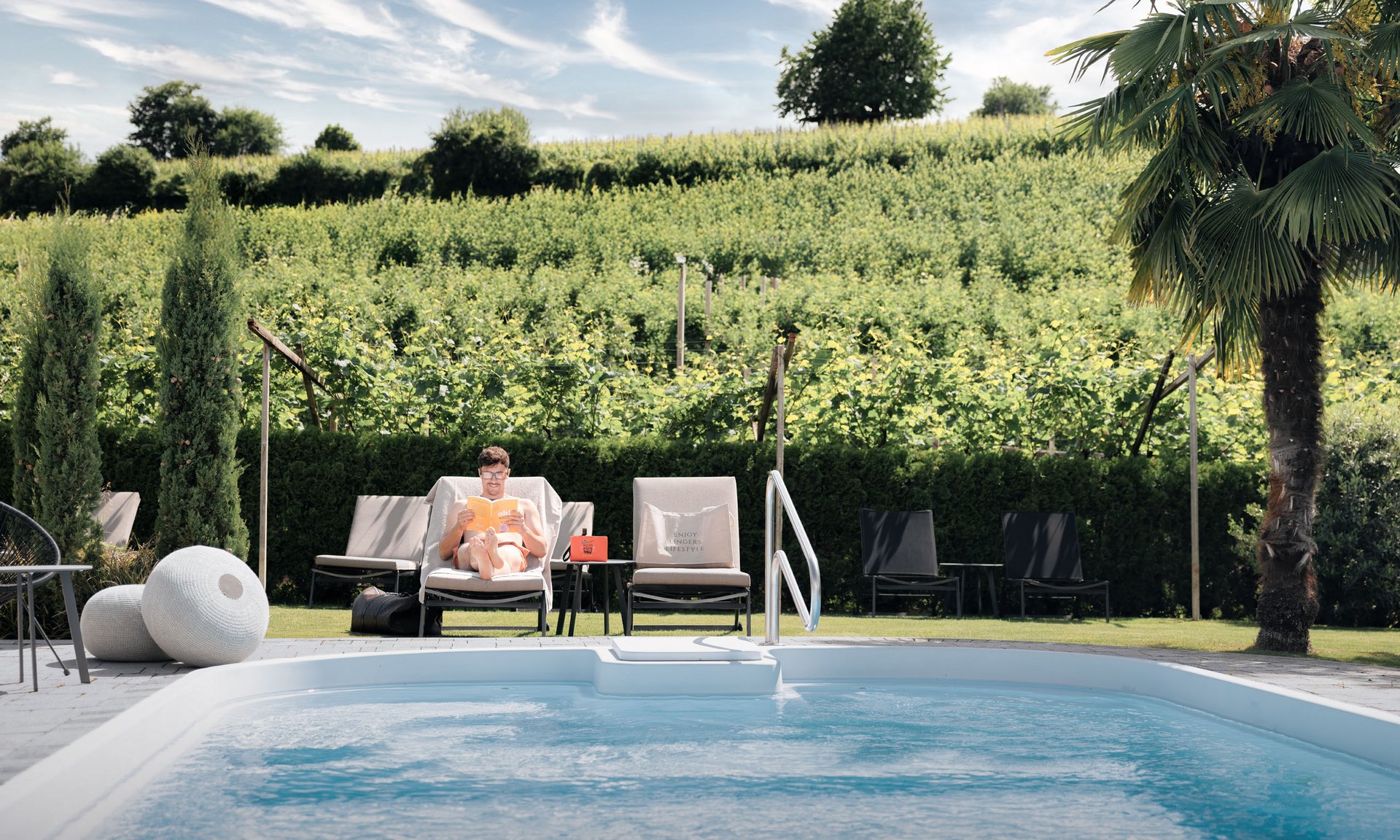 Lingers’ best snapshots Man reading on a lounge chair by pool with green vineyards in the background