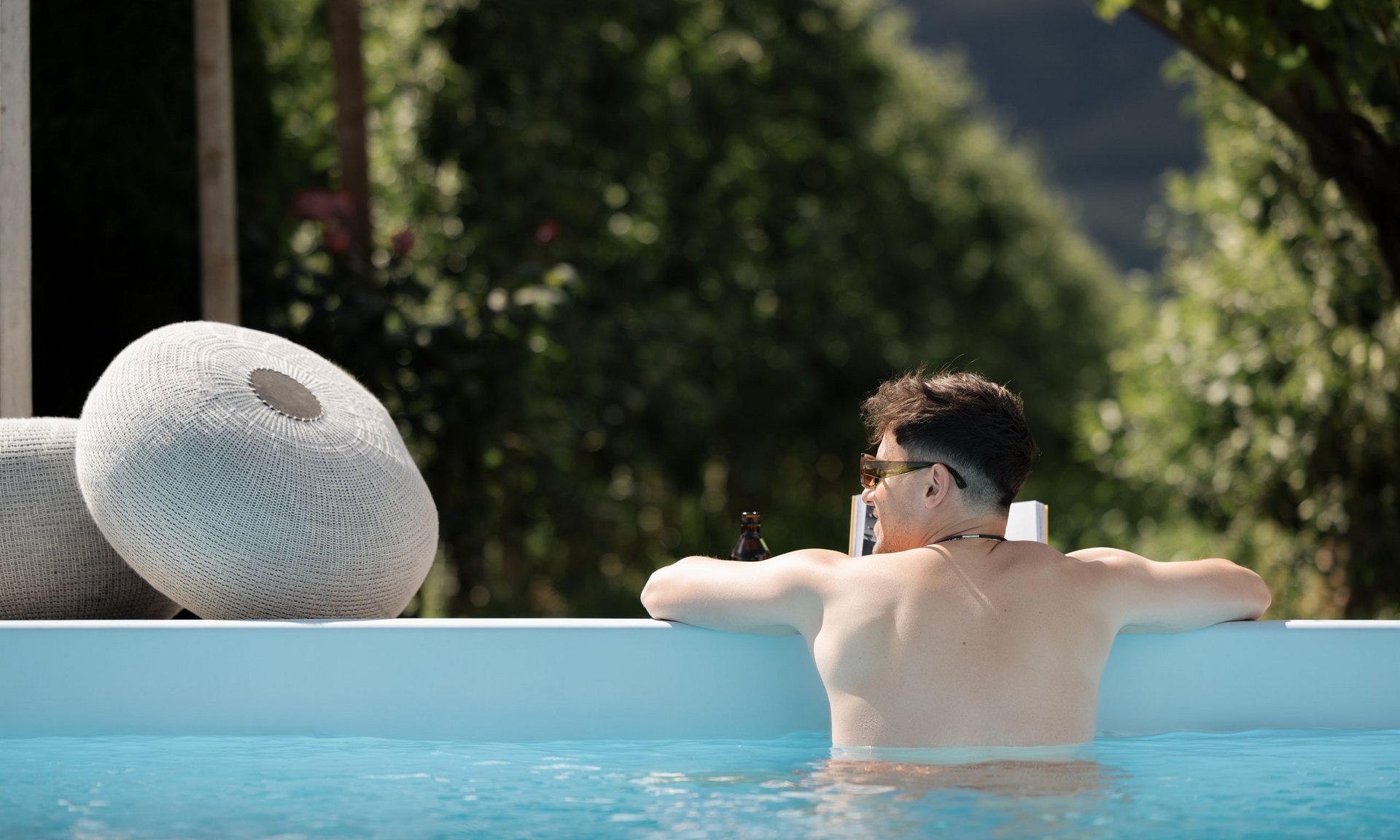 Lingers’ best snapshots Man relaxing in pool with book and drink surrounded by green nature