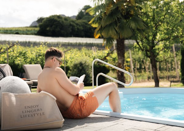 Lingers – Ihr Hotel in Girlan Mann in Badehose liest am Pool in der Sonne in ländlicher Umgebung