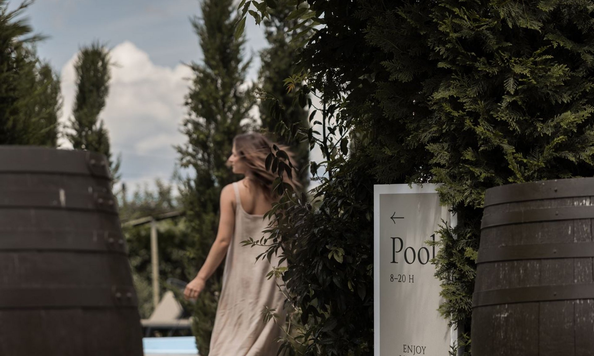 Lingers’ best snapshots Woman in light dress walking through green garden area towards pool