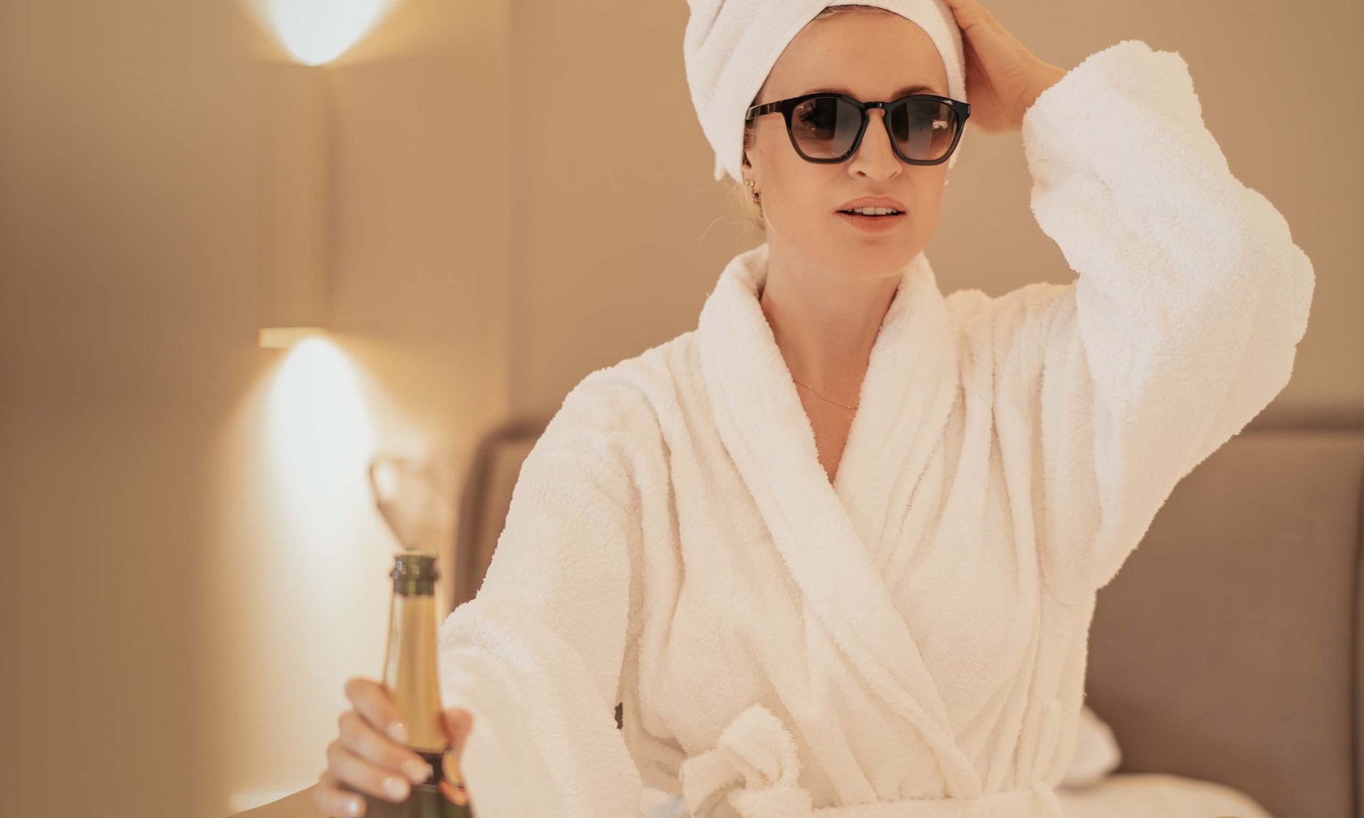 Lingers’ best snapshots Woman in bathrobe with sunglasses holding a champagne bottle on bed