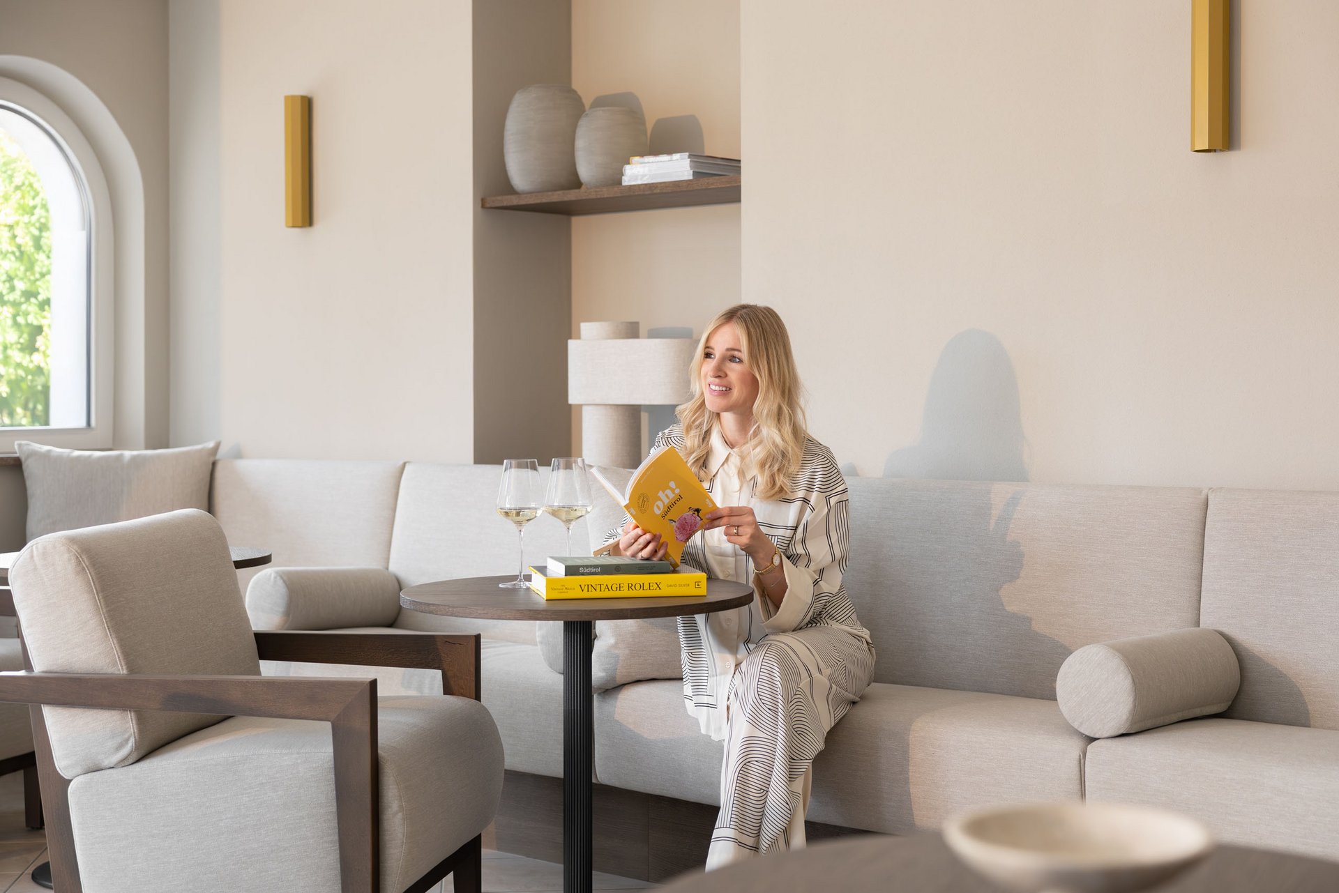 Lingers – Ihr Hotel in Girlan Frau liest Buch an Tisch mit zwei Weingläsern in gemütlichem Raum