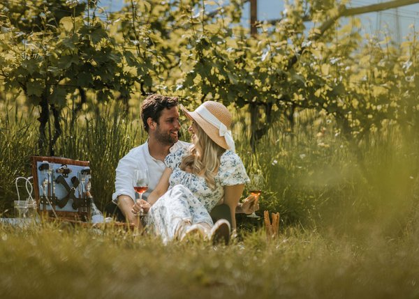 Lingers – Ihr Hotel in Girlan Paar beim Picknick im Weinberg mit Wein und Picknickkorb