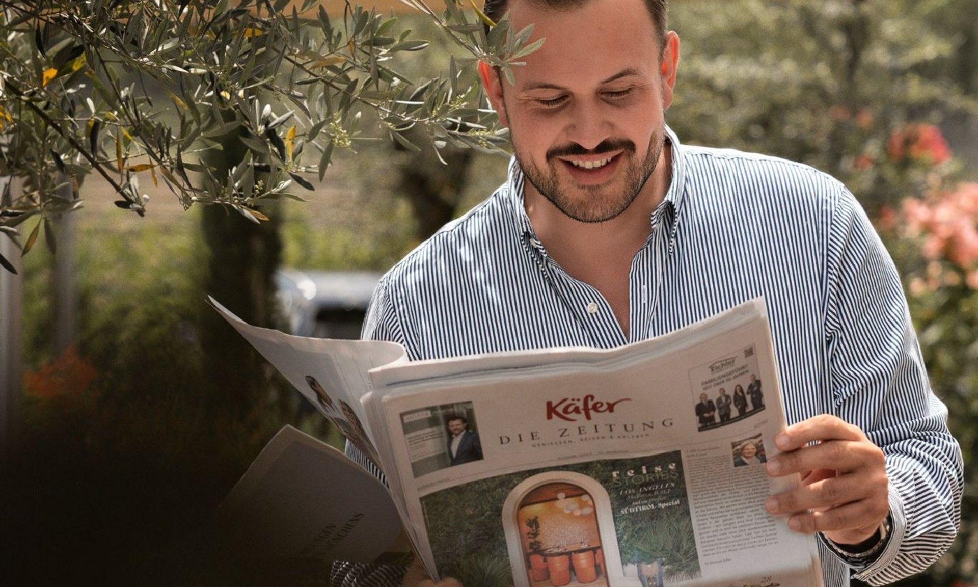 Lingers’ best snapshots Man reading newspaper outdoors under umbrella near olive tree