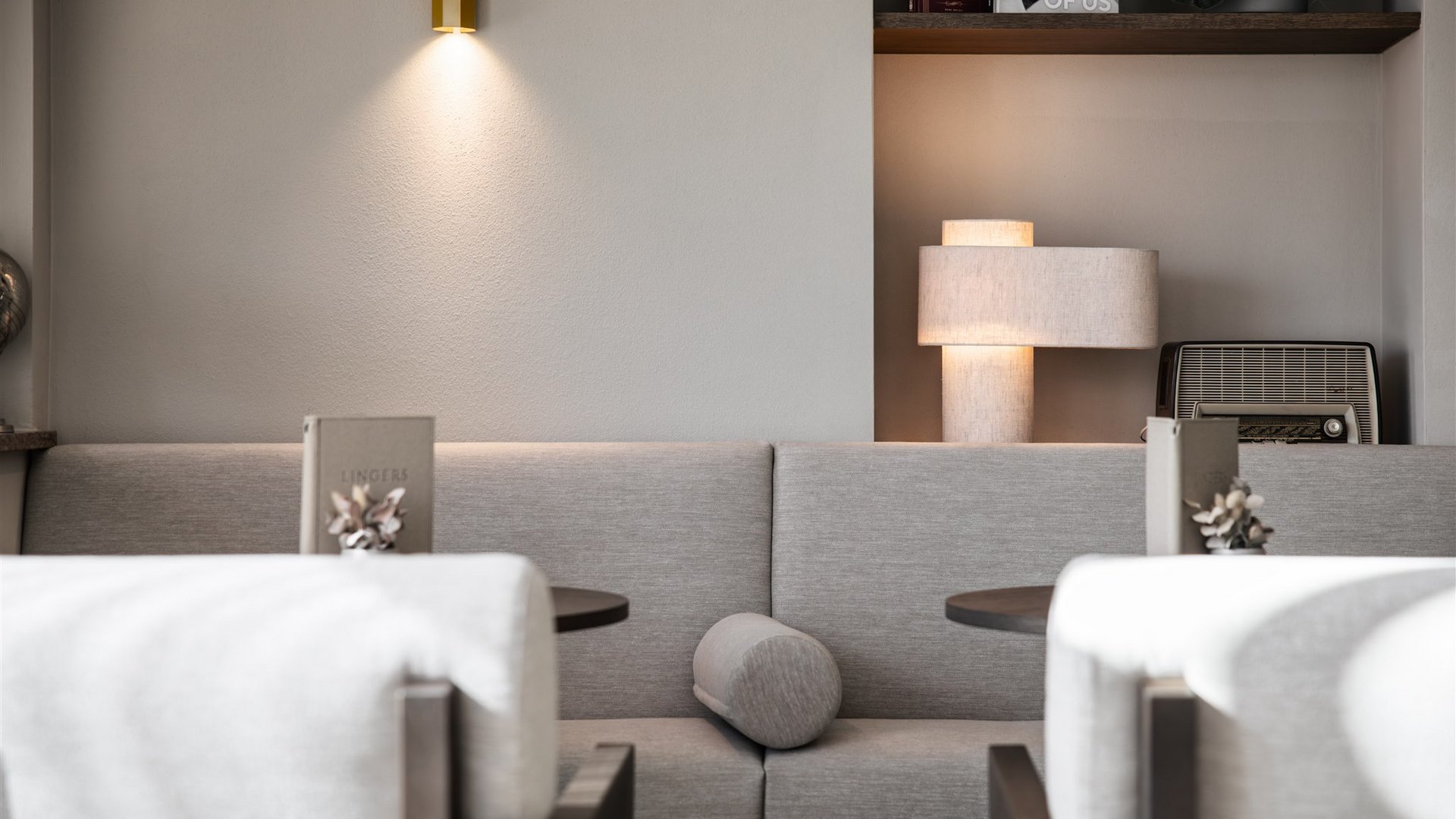 Lingers – Ihr Hotel in Girlan Moderner Sitzbereich mit grauem Sofa, zwei Tischen und sanfter Beleuchtung